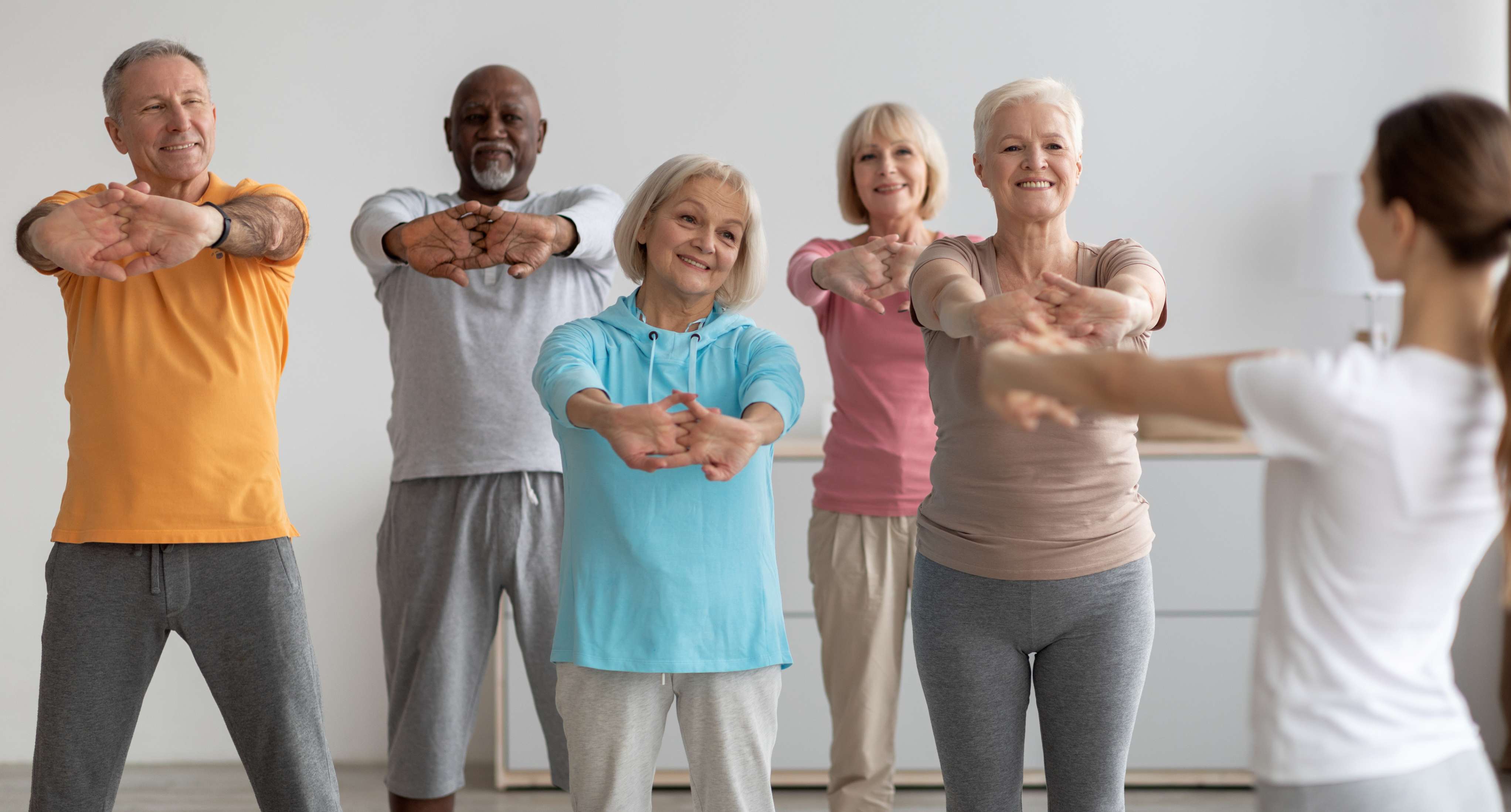 Group of older adults standing indoors and stretching their arms forward together during a guided balance and strength exercise class.